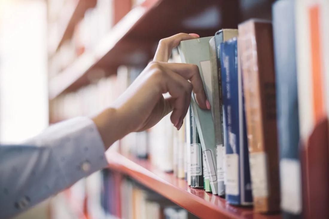 Hand greift nach einem Buch im Regal